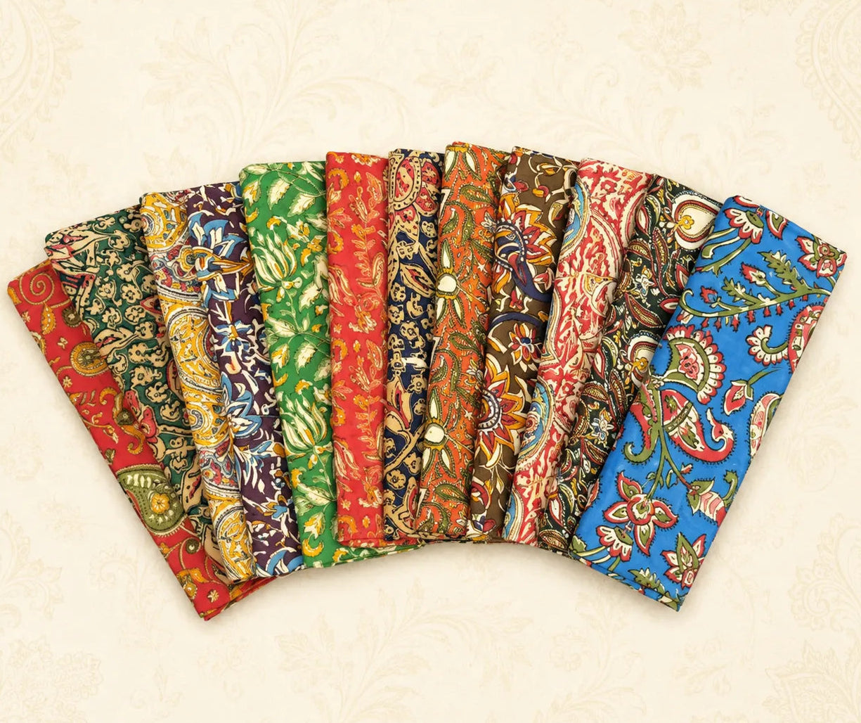 A fan arrangement of multiple batik fabric pieces in various colors and patterns, including red, green, blue, orange, and brown, displayed on a light beige patterned background.
