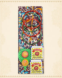 A colorful traditional Indian toy set featuring a patterned fabric board, red and green rings, a green and red ball, and two Triveni mouth freshener packets, arranged on a cream-colored patterned background.