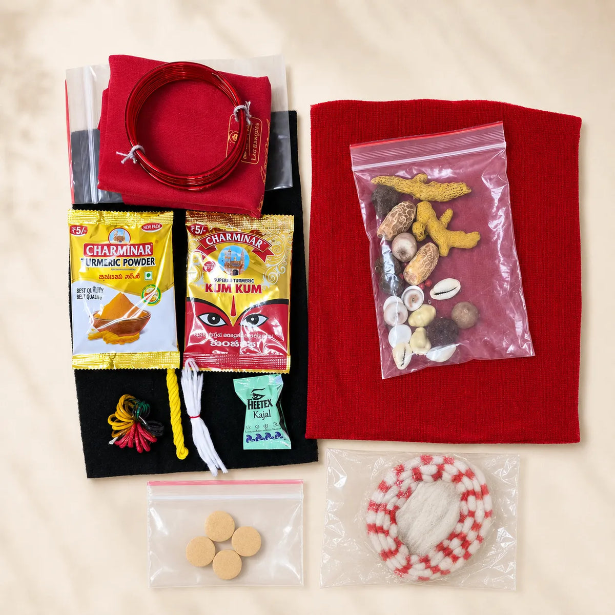 A flat-lay display of a traditional Indian folk art or dance costume kit on a light beige background. The kit includes a red felt dress, a red waist rope, a black felt skirt, colorful thread, Charminar spice powder packets, a small beaded necklace, and several small plastic bags containing accessories.