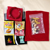 A flat-lay view of a traditional Indian matchmaking or ritual kit on a beige fabric background. The kit includes a red felt cloth, a red coiled cord, a black felt cloth with colorful tassels, two packets of Charminar Turmeric Powder, a packet of KJM Kum, a small packet of Hetta Clay, and a clear plastic bag containing various nuts, seeds, and spices.